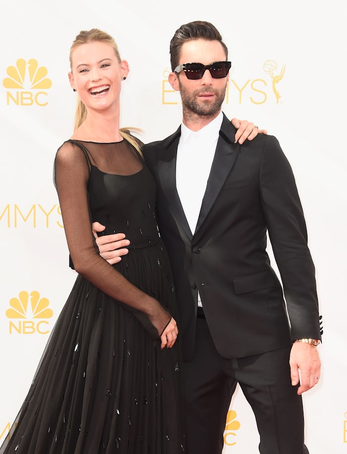 Adam Levine in a suit and sunglasses & Behati Prinsloo in a black dress posing on a red carpet 
