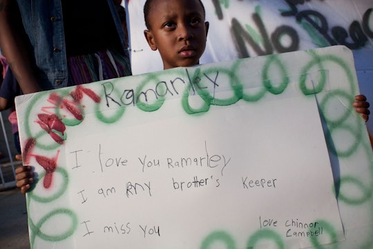 A black kid protesting against gun violence with "I love you Ramarley" banner