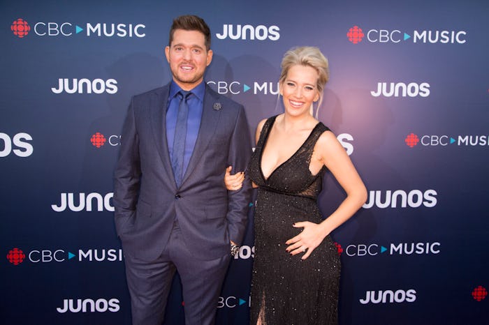 Michael Bublé in navy suit and a blue shirt, and his wife in a black dress at a red carpet event