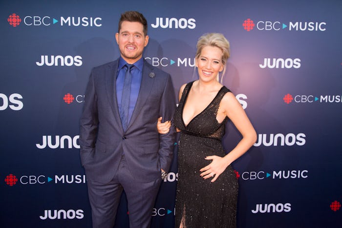 Michael Bublé in navy suit and a blue shirt, and his wife in a black dress at a red carpet event
