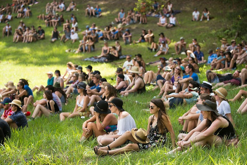 A group of students wearing sun protective hats sitting on a grass in a shade