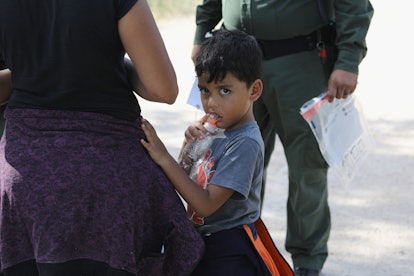 An immigrant child looking at the camera while having his hand on his mother