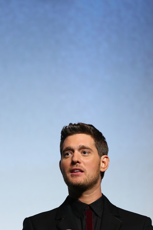 A portrait of Michael Buble in a black shirt and a black blazer with a blue background
