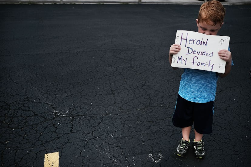 A boy holding a poster with the text 'Heroin Divided My Family'