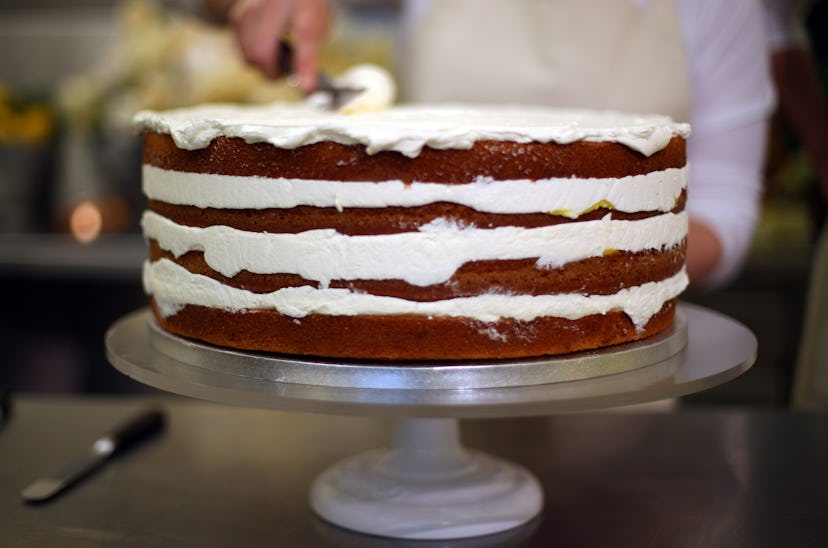 A carrot cake on a cake stand being decorated with frosting