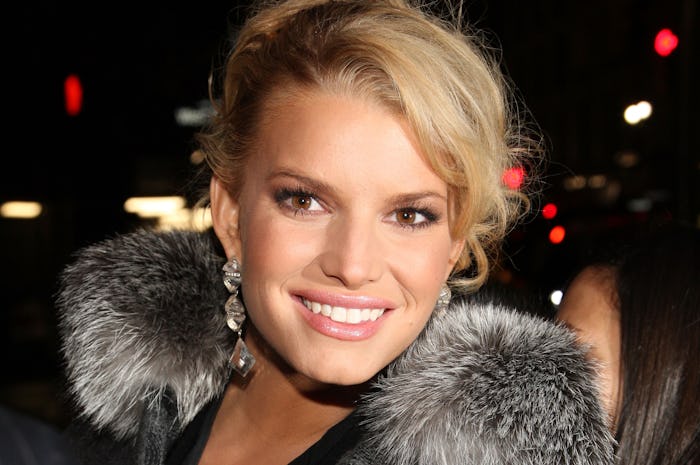 A close-up portrait of Jessica Simpson with large earrings and a fur collar
