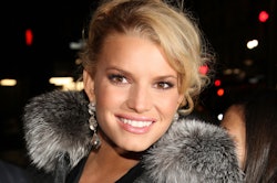 A close-up portrait of Jessica Simpson with large earrings and a fur collar
