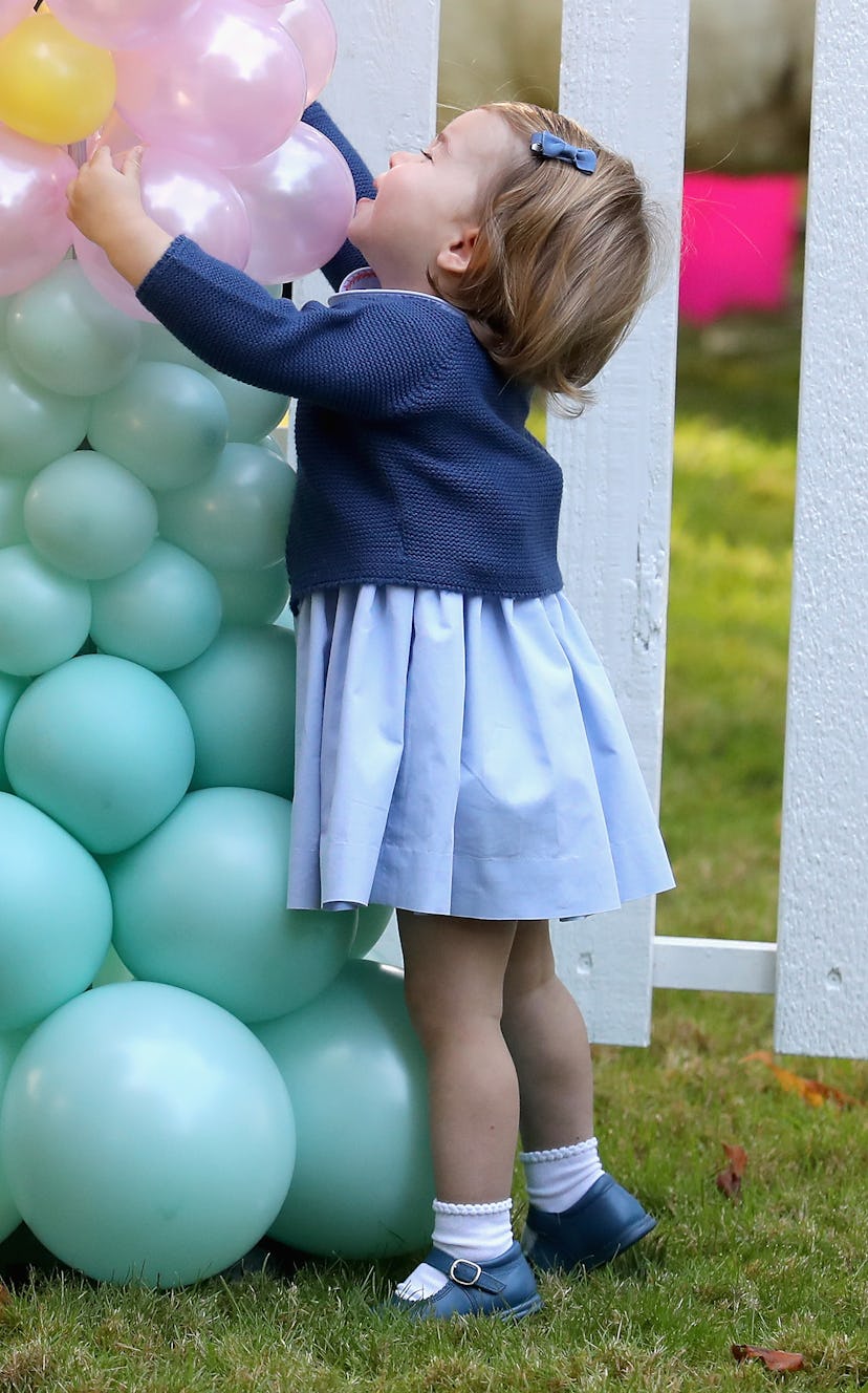 Princess Charlotte hugs a wall of balloons at a tea party. 