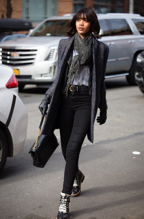 A woman wearing a long grey knitted scarf, matching coat, and black pants.