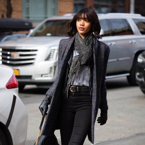 A woman wearing a long grey knitted scarf, matching coat, and black pants.
