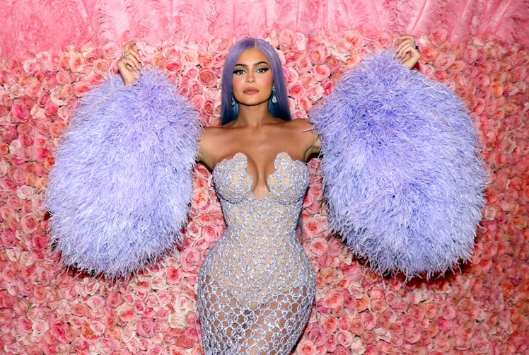 Kylie Jenner poses in front of a rose wall at the 2019 Met Gala in a purple dress with fluffy purple...