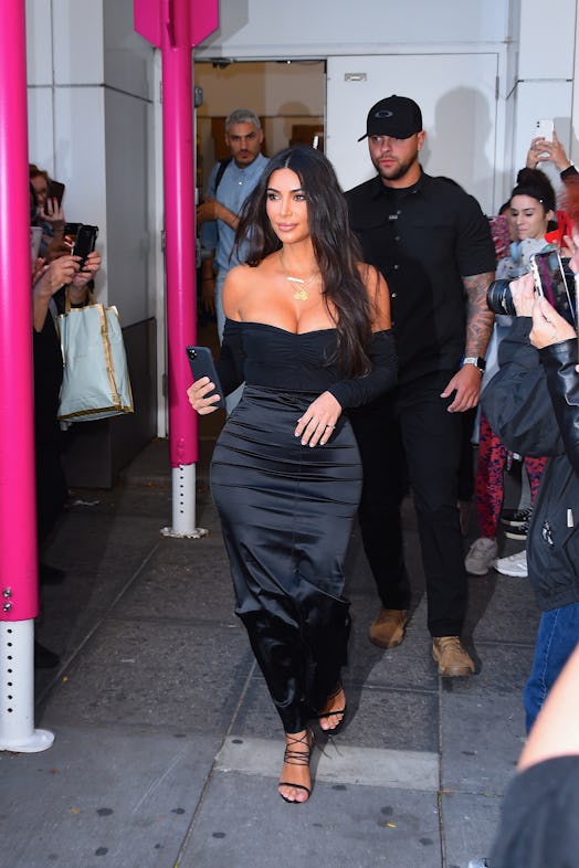 Kim Kardashian walks out of an event in a black skirt and long-sleeve shirt and heels.