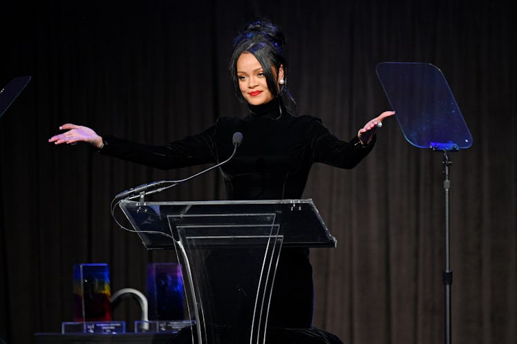 Rihanna stands at a podium with hands spread wide to the audience