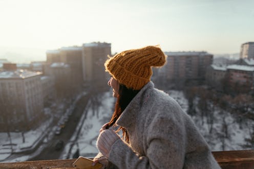 A woman in a hat looks out over a snowy cityscape. The winter solstice means that the days will soon...
