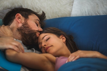 Una pareja duerme tranquilamente en la cama, mientras el hombre besa la cabeza de la mujer.'s head. 