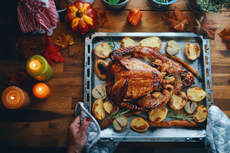 A woman holds tray of potatoes and turkey with stuffing on Thanksgiving table.
