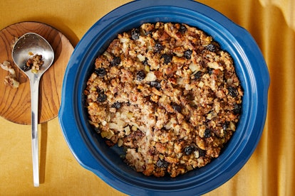 A bowl of stuffing is placed on a Thanksgiving table with a spoon next to it.