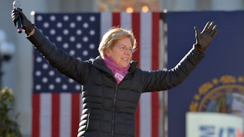 Elizabeth Warren in a black jacket with the American flag in the background