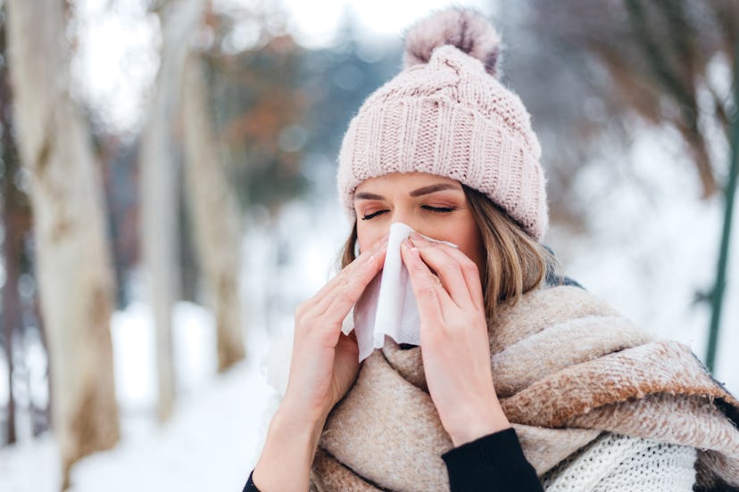 A woman blows her nose in a wintry landscape. Fluctuating hormones throughout the menstrual cycle ca...