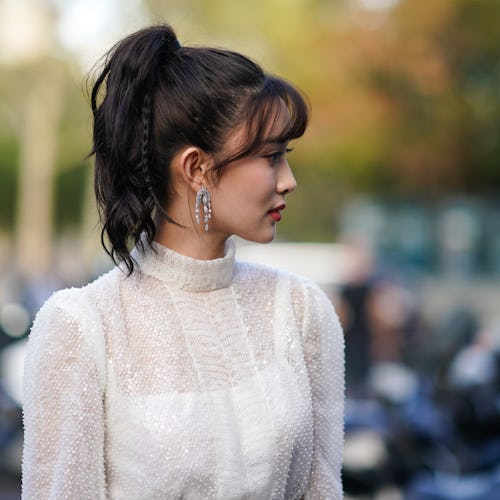 A woman posing in a sheer shite dress, and sparkly earrings with her hair in a ponytail