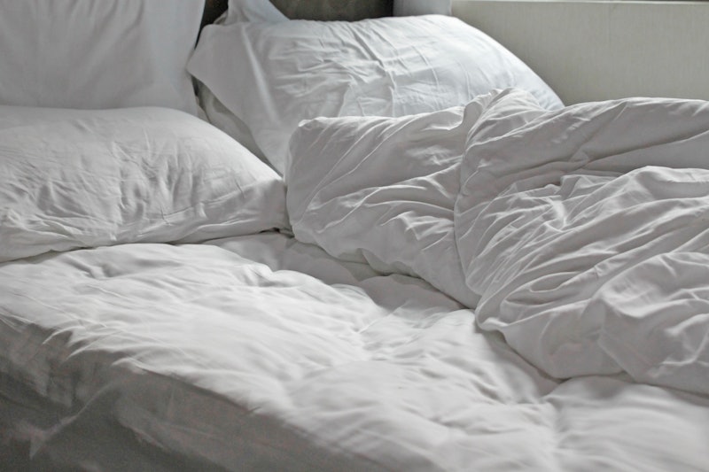 A white duvet on a white bedspread on an unmade bed. Allergies to bird feathers can be tough when so...
