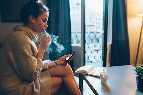A woman vapes while looking at her phone. Quitting vaping may have benefits for your body, but more ...