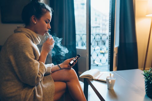 A woman vapes while looking at her phone. Quitting vaping may have benefits for your body, but more ...