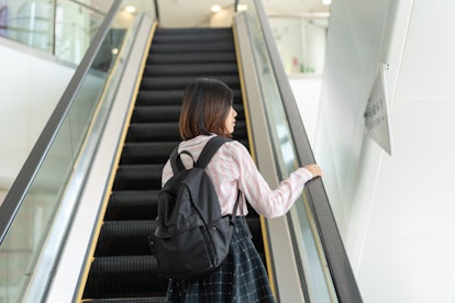 A woman rides an escalator in an airport. Hand rails, elevator buttons and other communal surfaces c...