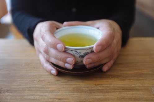 A pair of hands around a cup of green tea. Green tea comes in many varieties, and switching to green...