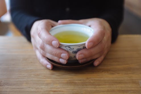 A pair of hands around a cup of green tea. Green tea comes in many varieties, and switching to green...