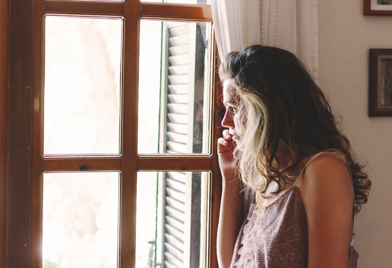 A brunette woman standing next to a window and talking on the phone about addiction