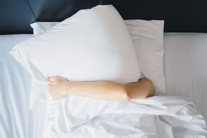 Lady lying down in her bed and covering her face with a pillow