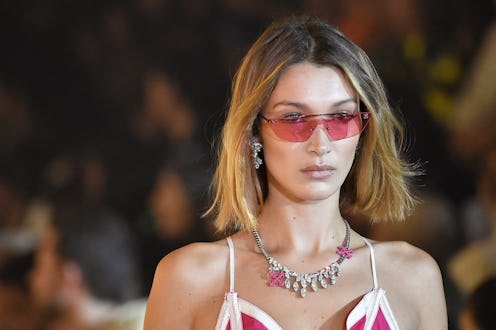Bella Hadid in rose tinted sunglasses, a necklace and a red and white strap top