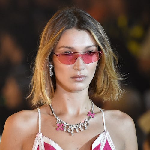 Bella Hadid in rose tinted sunglasses, a necklace and a red and white strap top