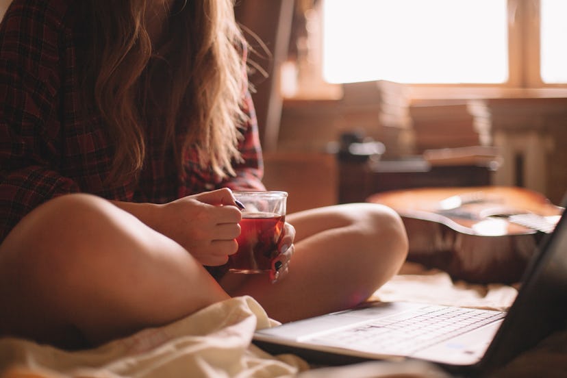 A woman watches TV on her laptop and drinks tea. Marathon watching may be linked to anxiety, but wha...