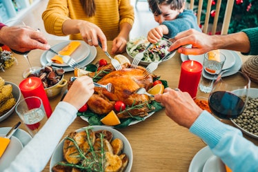 A family surrounds a Thanksgiving dinner table and sticks their forks into the turkey in the middle.