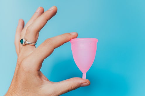 A left hand holding a pink menstrual cup