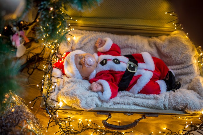 a newborn baby in a santa suit posed with Christmas lights