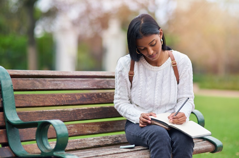 A woman on a bench writes her to-do list in a notebook so she can stop forgetting things.