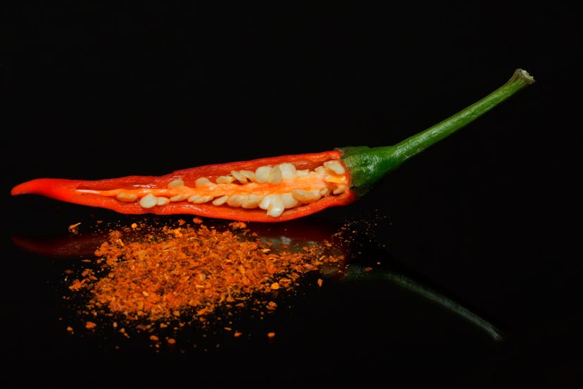 A chili pepper, cut in half long-ways against a black background, revealing fresh seeds inside and a...