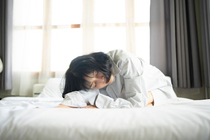 A woman curls up sleeping on a bed. Alcohol can have many effects on sleep, all of which reduce slee...