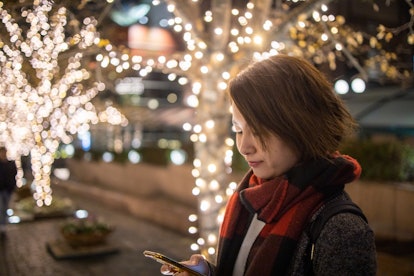 A woman types on her phone in front of Christmas lights. A support network of family and friends can...