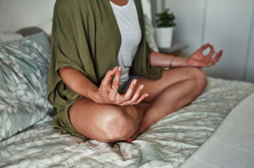 A woman sits in lotus pose on a bed. Workout out at home when you're stuck at your parents' house ov...