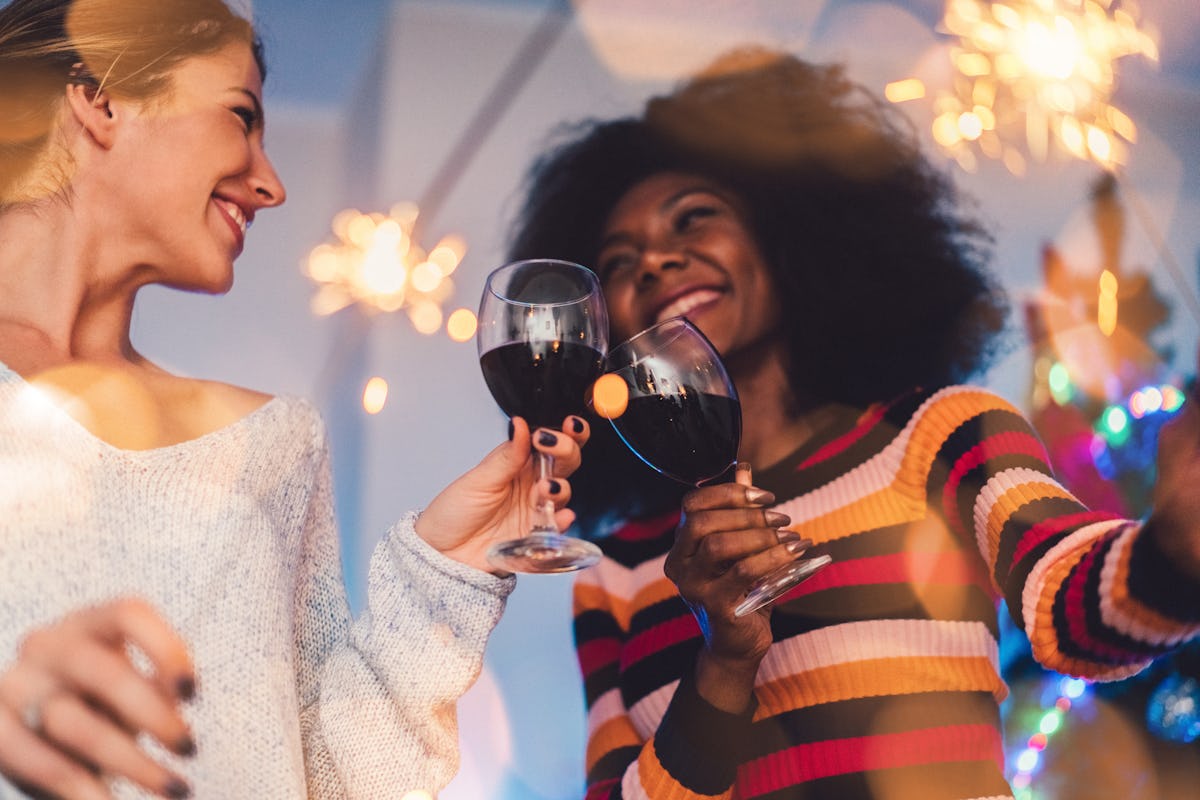 Two girl friends clink their wine glasses and hold sparklers on New Year's Eve.