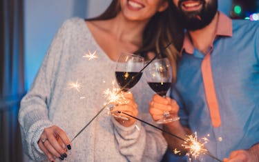 Ein Paar Toasts ihre Rotweingläser und halten Wunderkerzen am Silvesterabend.