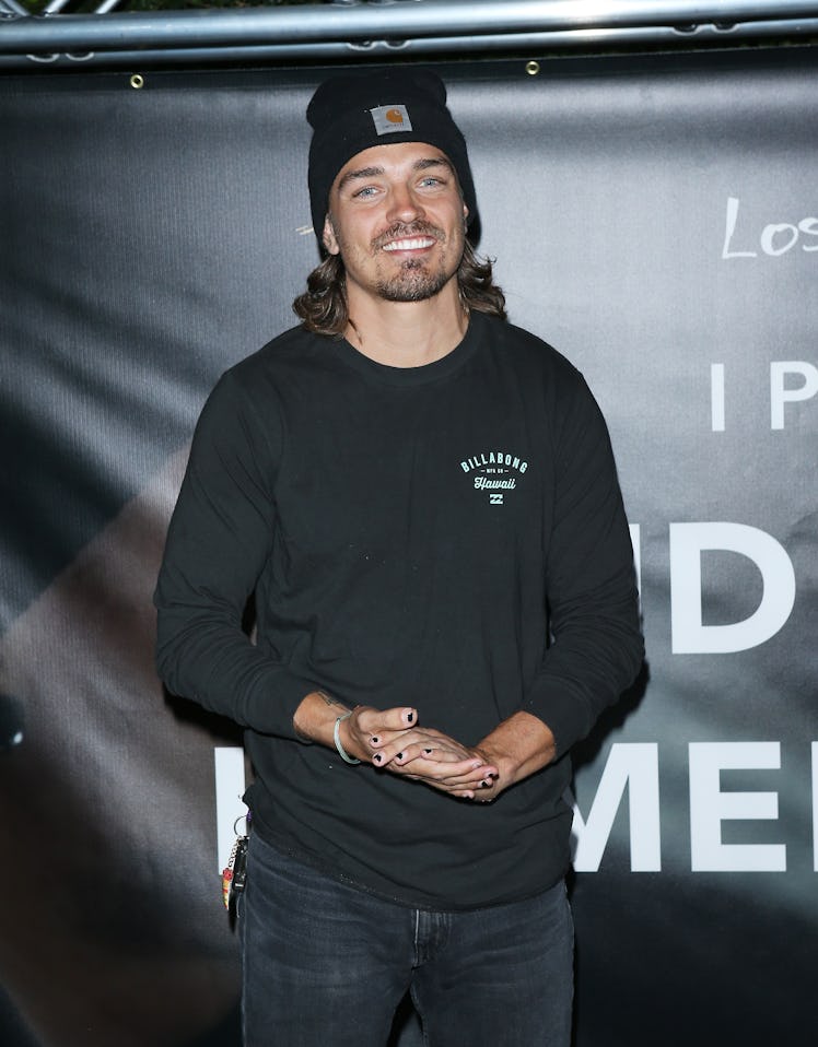 Dean Unglert wears a black beanie, black T-shirt, and jeans in front of a black backdrop.