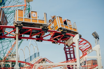 The orange cart of a coaster in Coney Island zooms down its red track.