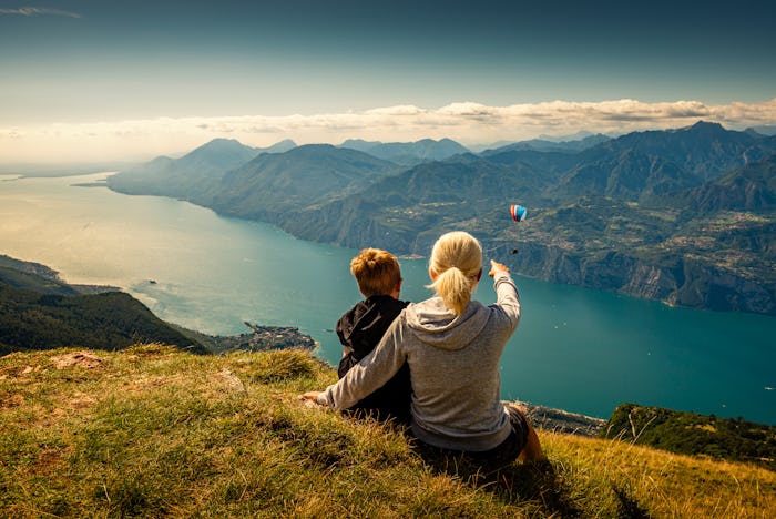 a woman and boy looking at a skydiver over a river