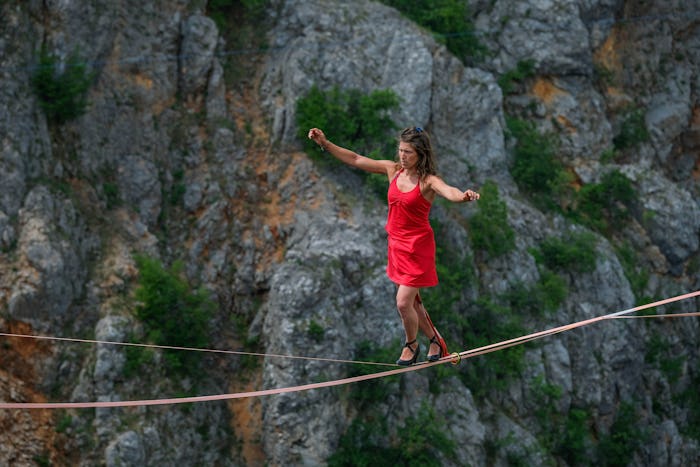woman walking a tightrope in heels between cliffs