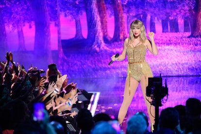 Taylor Swift wearing a golden-colored bodysuit on a stage in front of the crowd